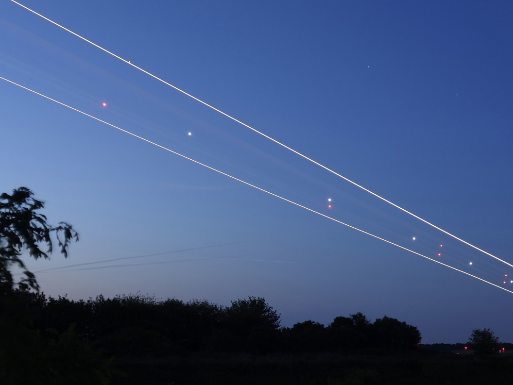 Lang eksponering av stjerneklar himmel med flylys i bevegelse over natthimmel, omgitt av skogkledd horisont