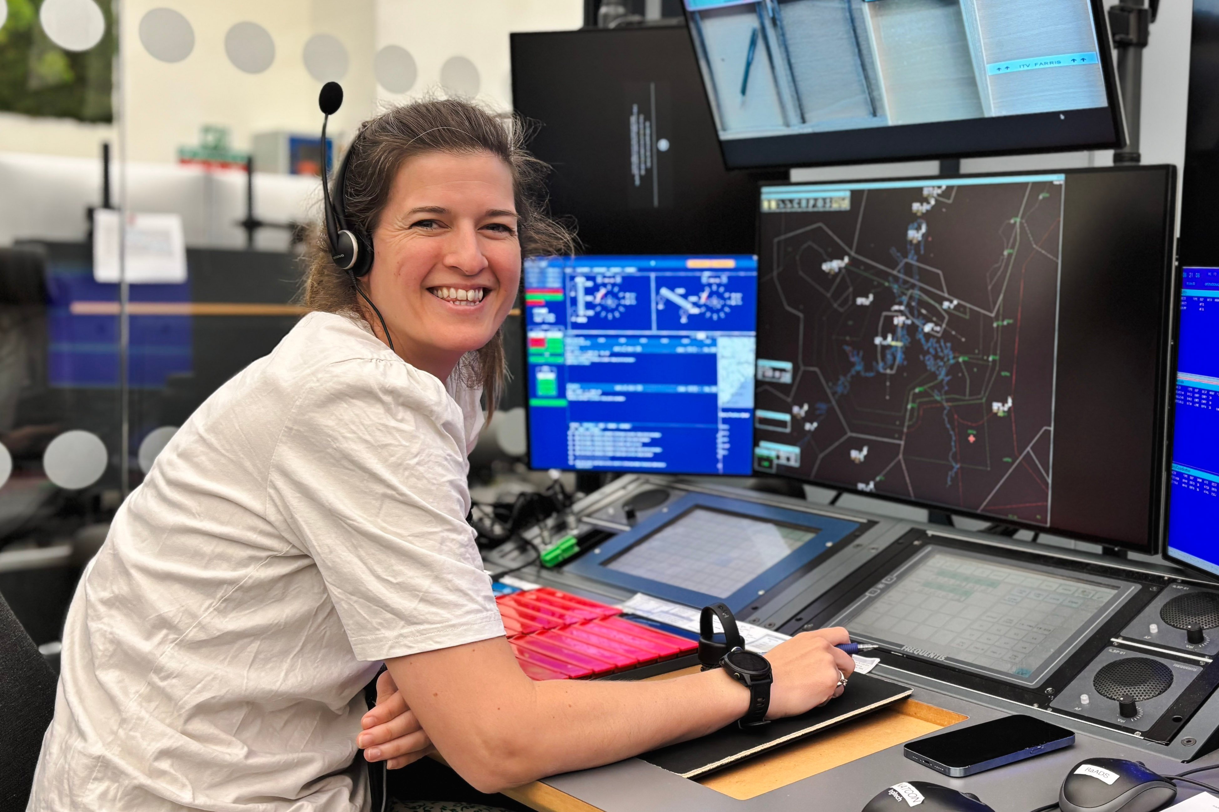 Kvinne med headset jobbar på kontrollsenter, ser på fleire dataskjermar med informasjon og kart