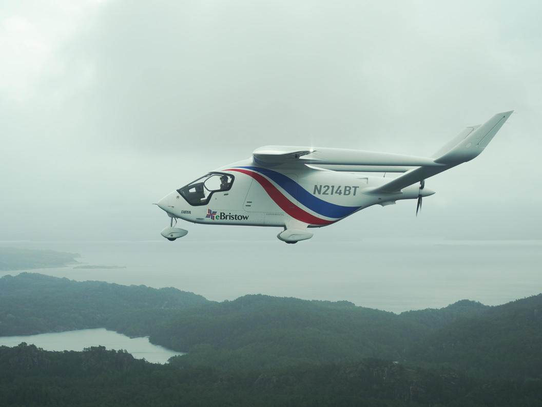 Electric plane with Bristow logo flying over scenic landscape and water under a cloudy sky.