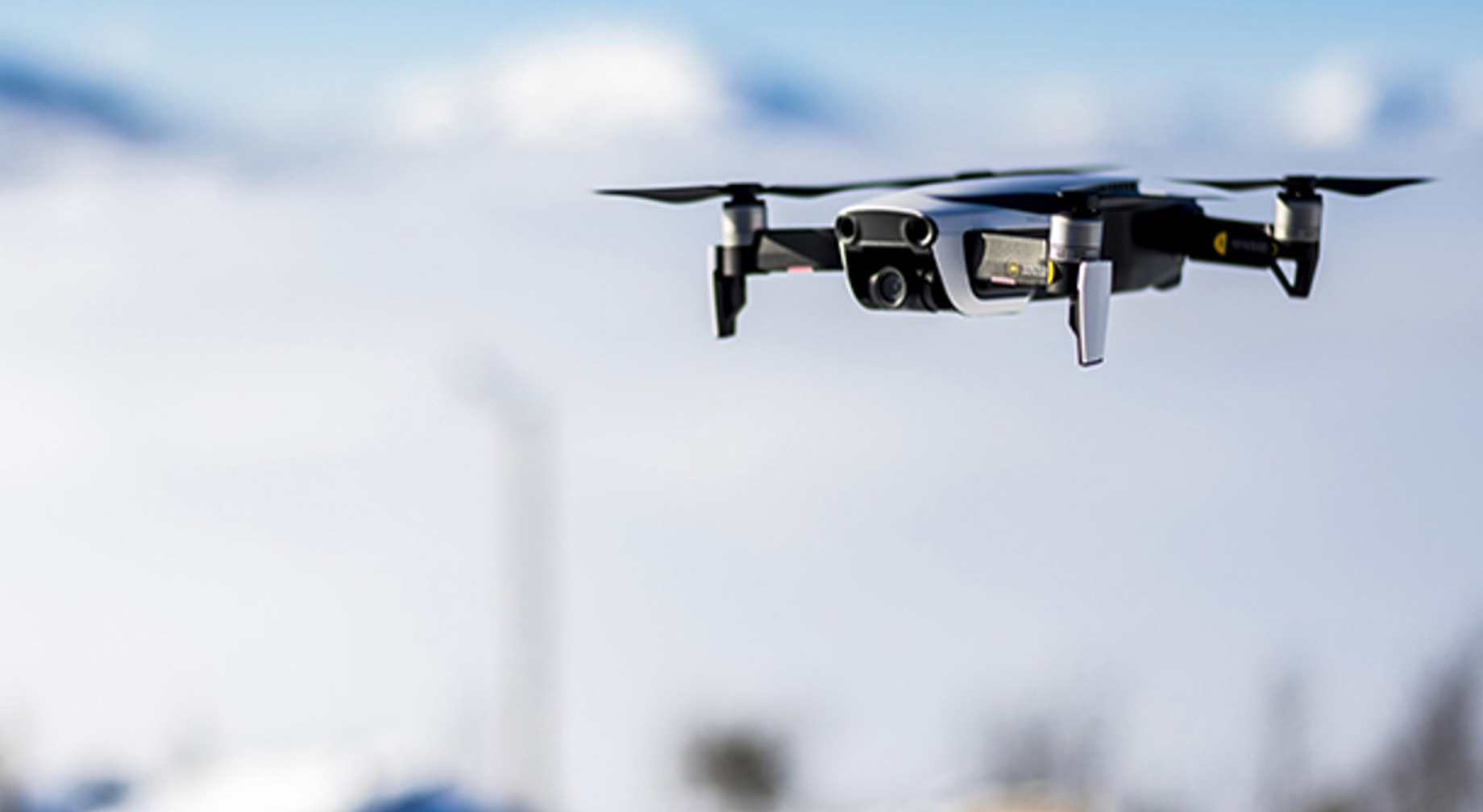 Drone flygande høgt over snødekte fjell med blå himmel i bakgrunnen